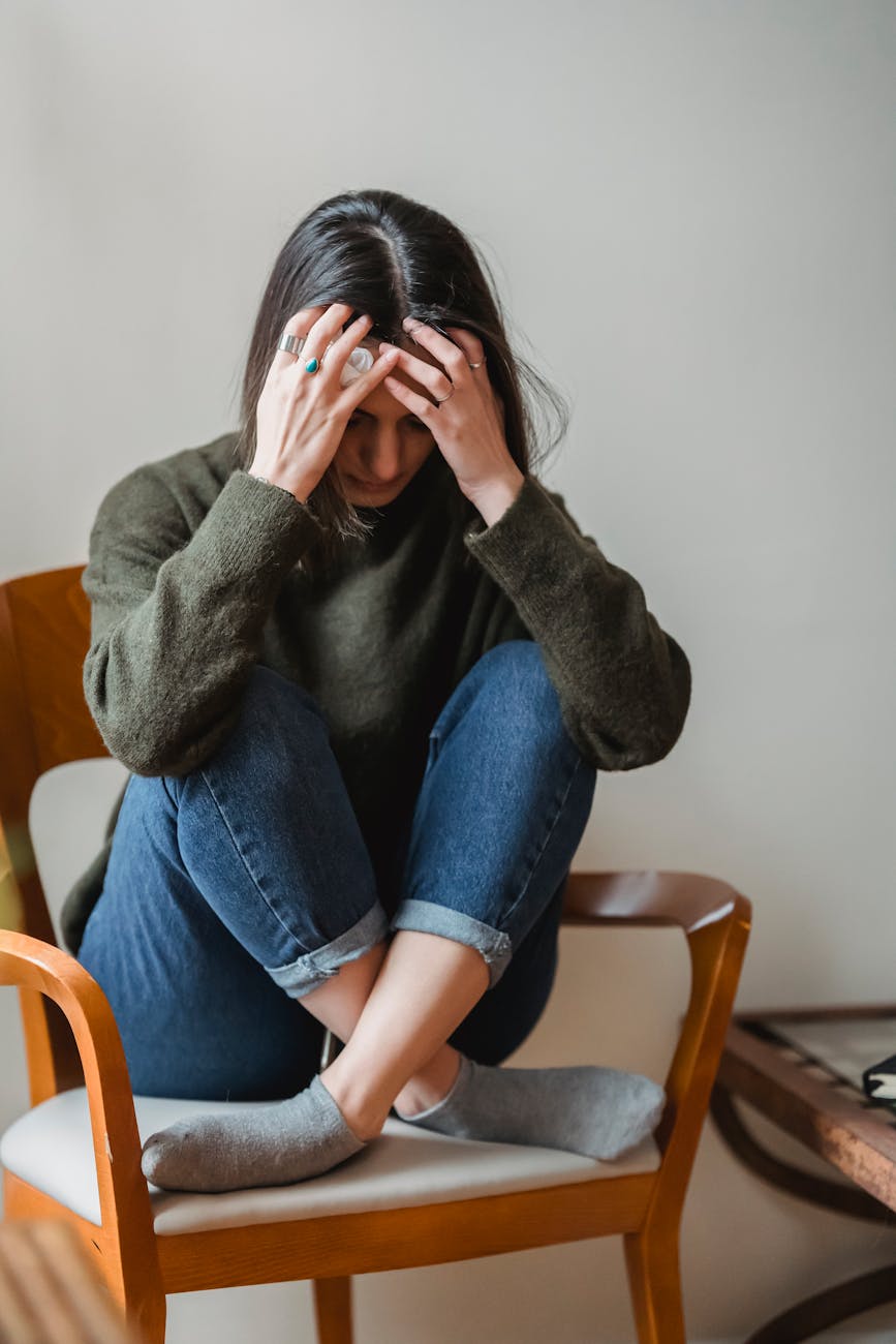 stressed young ethnic woman grabbing head while sitting on chair